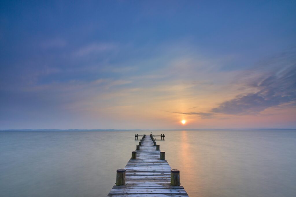 Serene sunrise over a tranquil lake with a wooden pier leading into the distance.