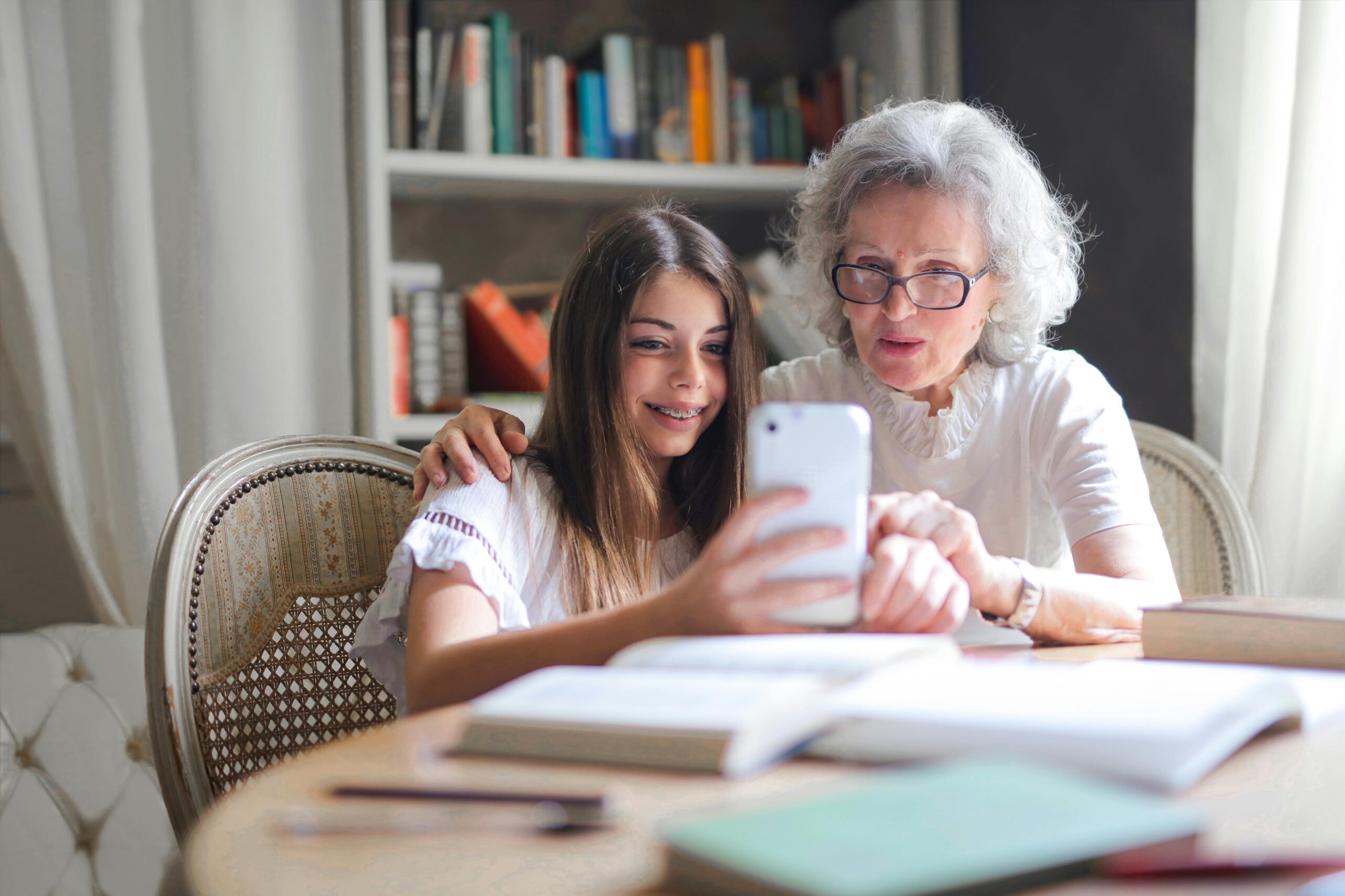 A grandmother and granddaughter bonding over a smartphone at home, showcasing generational connection.